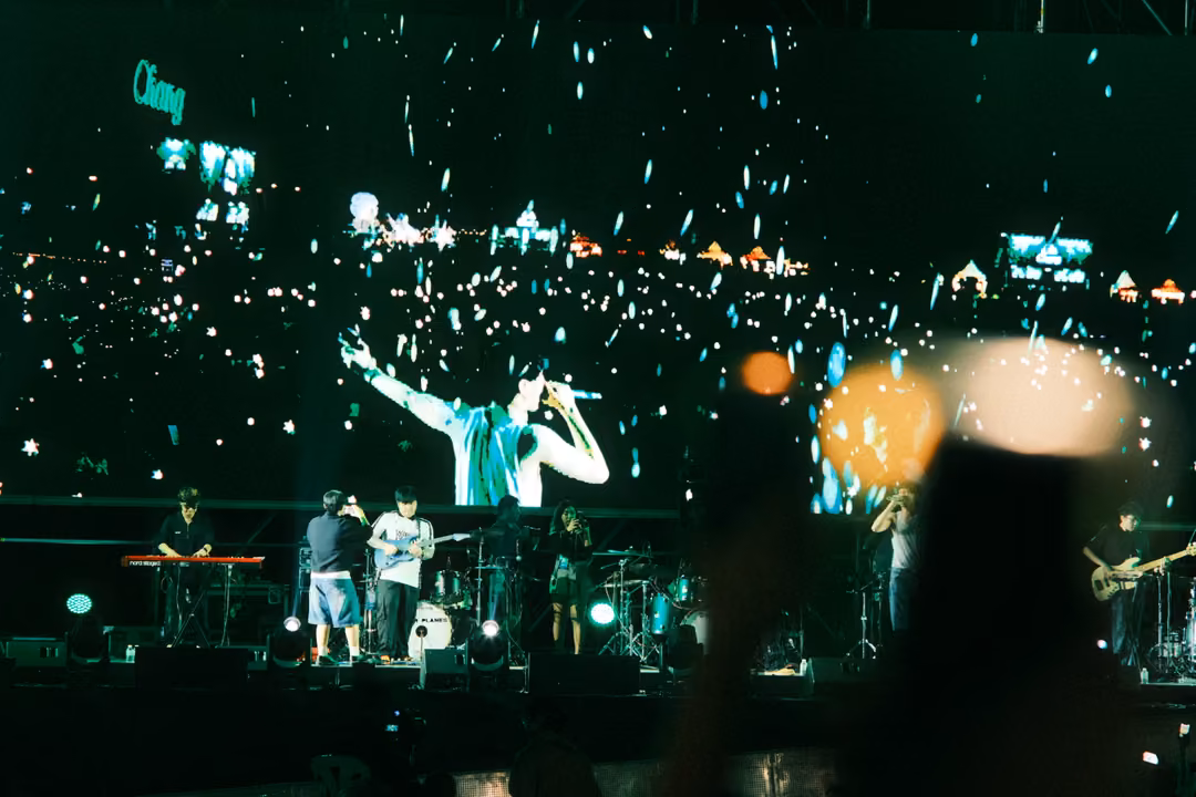Screen showing the singer with arms outstretched before a sea of phone lights, blurred hands waving in the foreground.