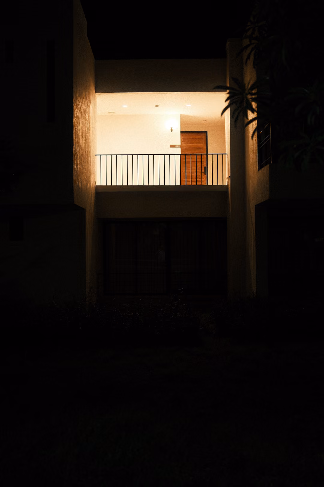 A villa facade at night with only an upper balcony and doorway lit, the rest in darkness