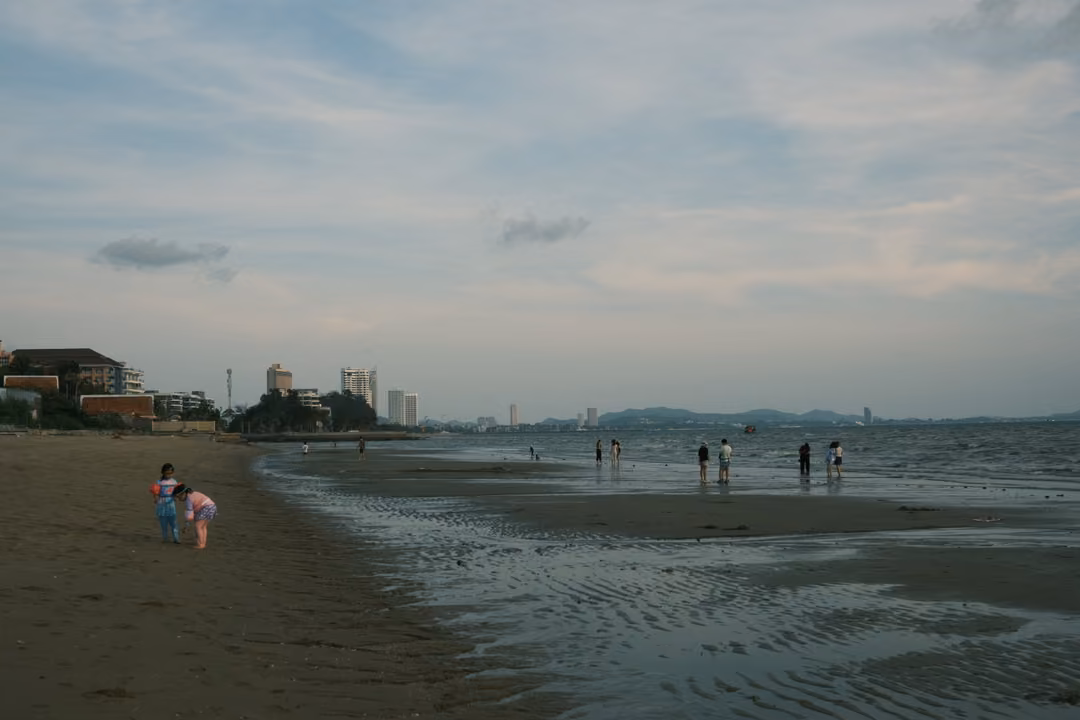 A wide beach at low tide with rippled wet sand, people wading far out and a distant coastline