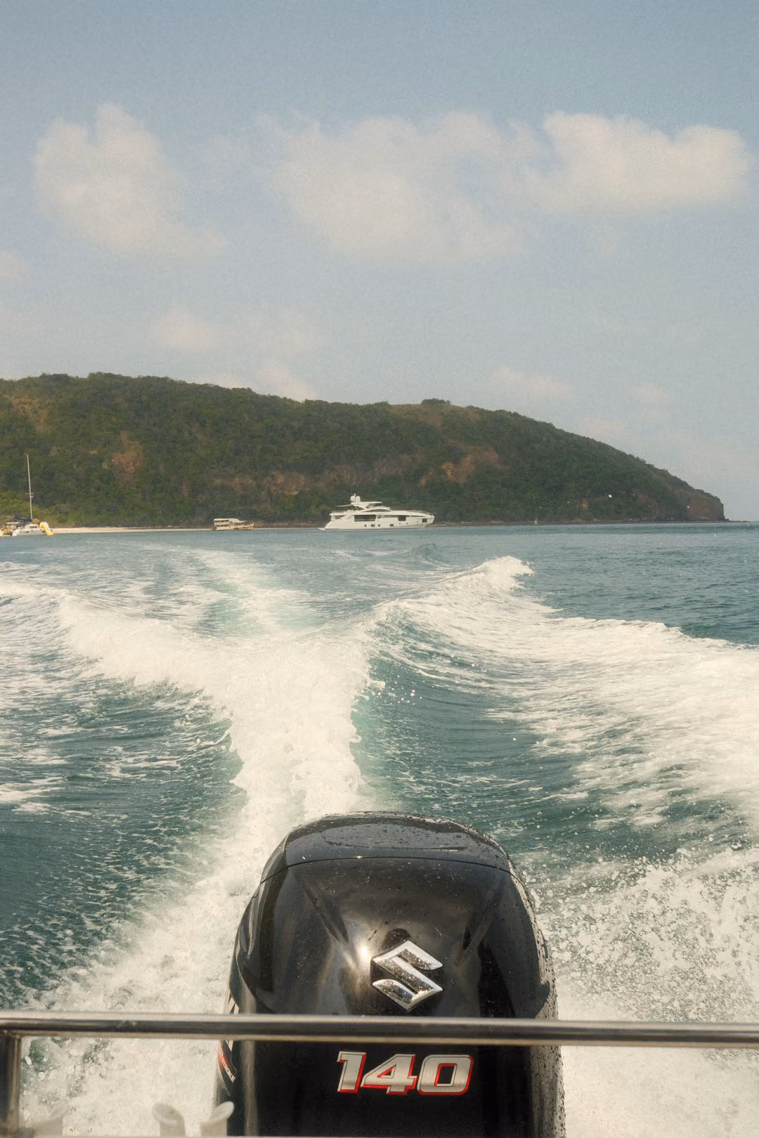 The outboard motor marked 140 churning a white wake toward a green island with a white boat.
