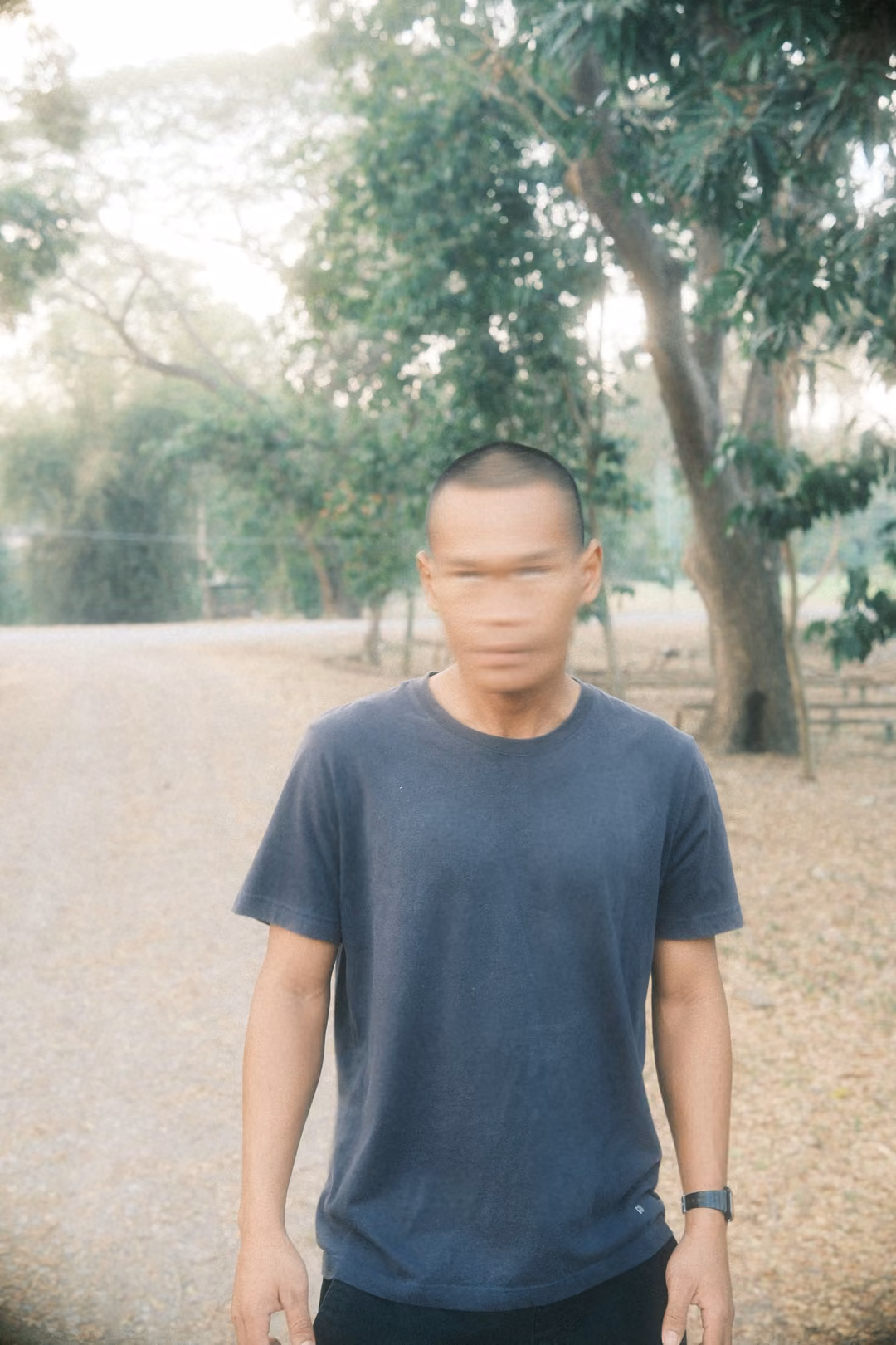 Man in a grey t-shirt standing on a gravel road among trees, his face smeared by motion blur