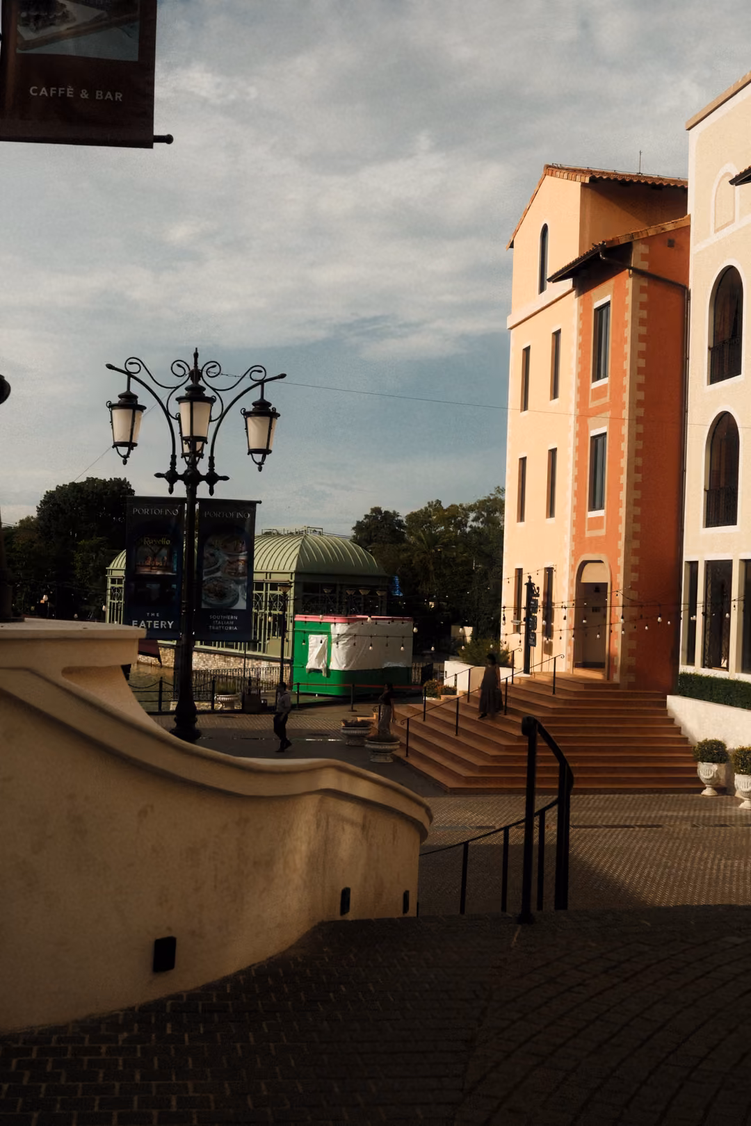 Ornate black street lamp beside a curved cream wall and stairs leading up to a peach building under cloudy sky