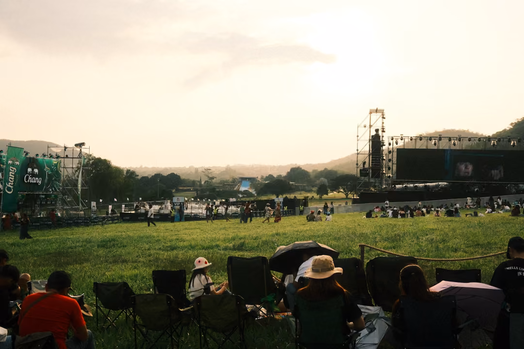 A wide grassy field with rows of chairs and umbrellas, green banners and a stage at the far end.
