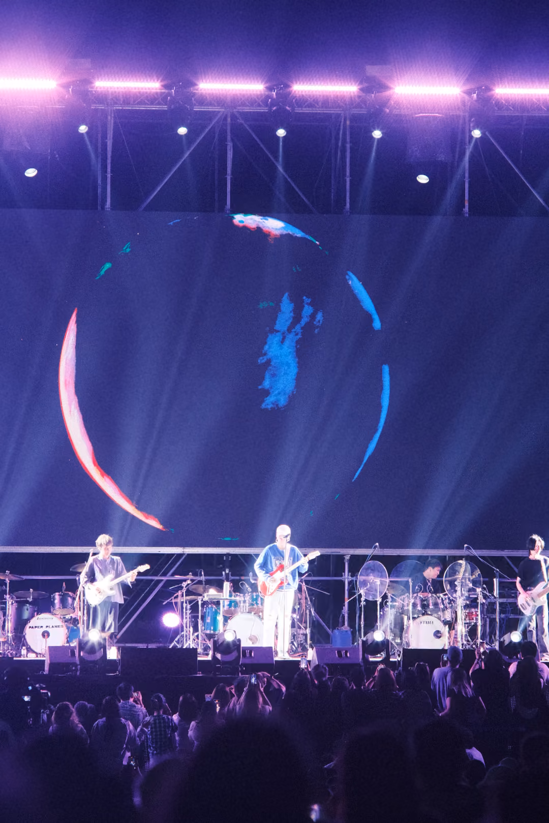 Vertical view of a screen where the red sphere has dissolved into a faint blue outline, band performing below.