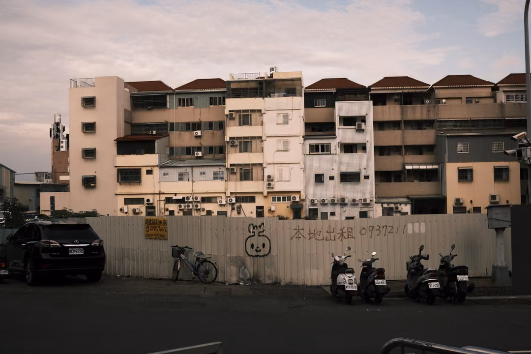 Apartment block behind a construction fence with painted characters, scooters and a bicycle parked in front