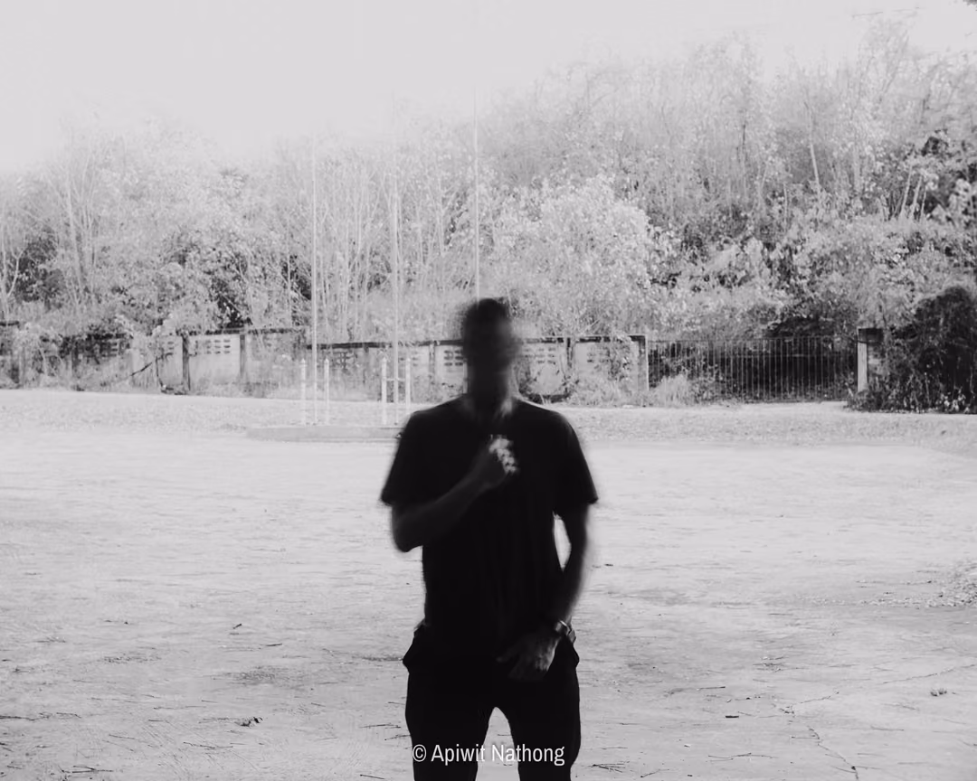 Black and white full-length figure in dark clothes with a blurred face standing on bare cracked ground