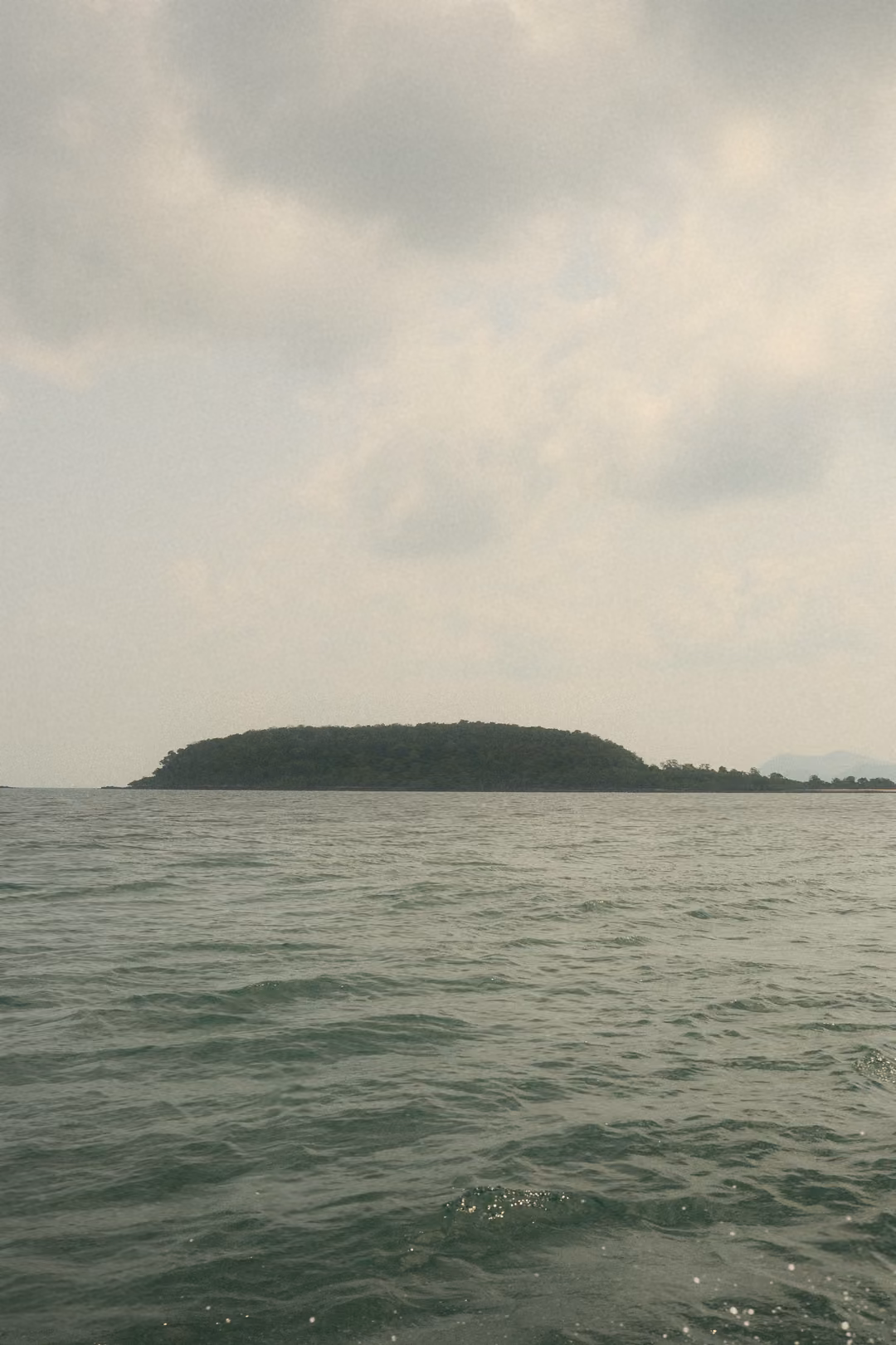 A low, dark green island on the horizon over grey-green sea beneath heavy cloud.