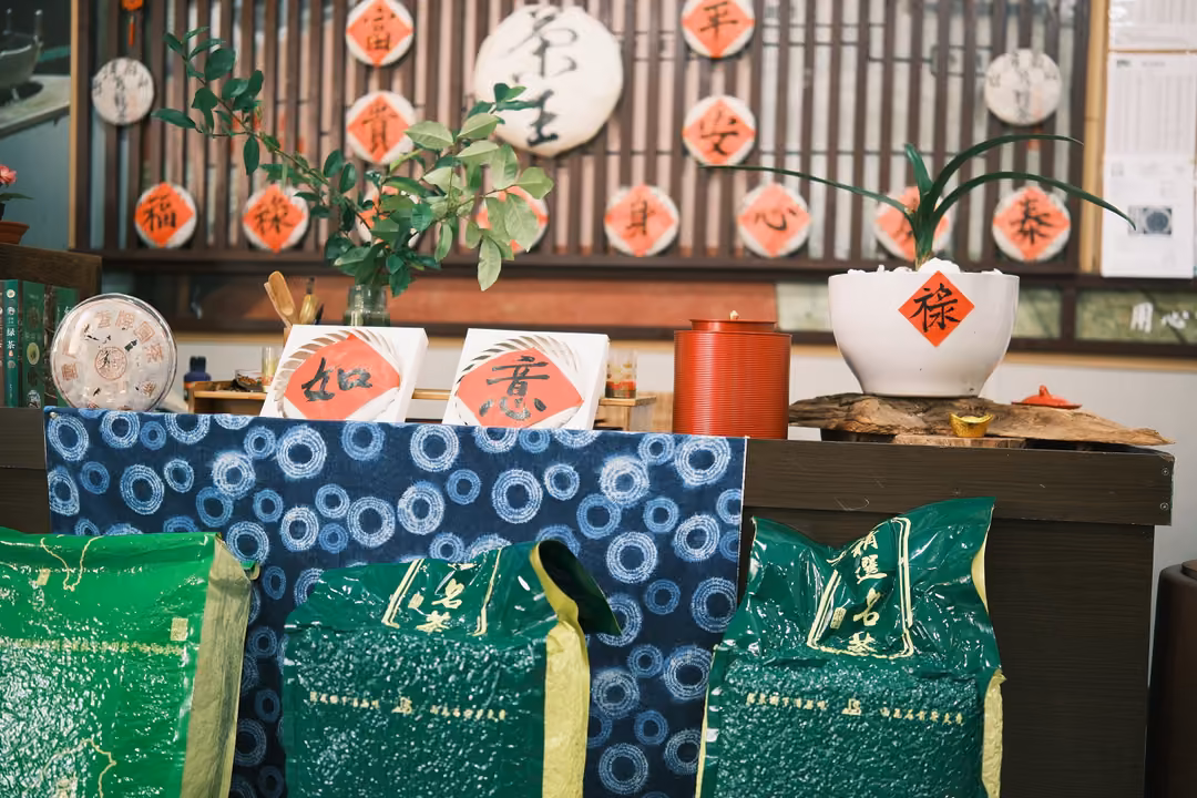Counter draped in blue patterned cloth with green tea bags, red character cards and a white planter marked 祿