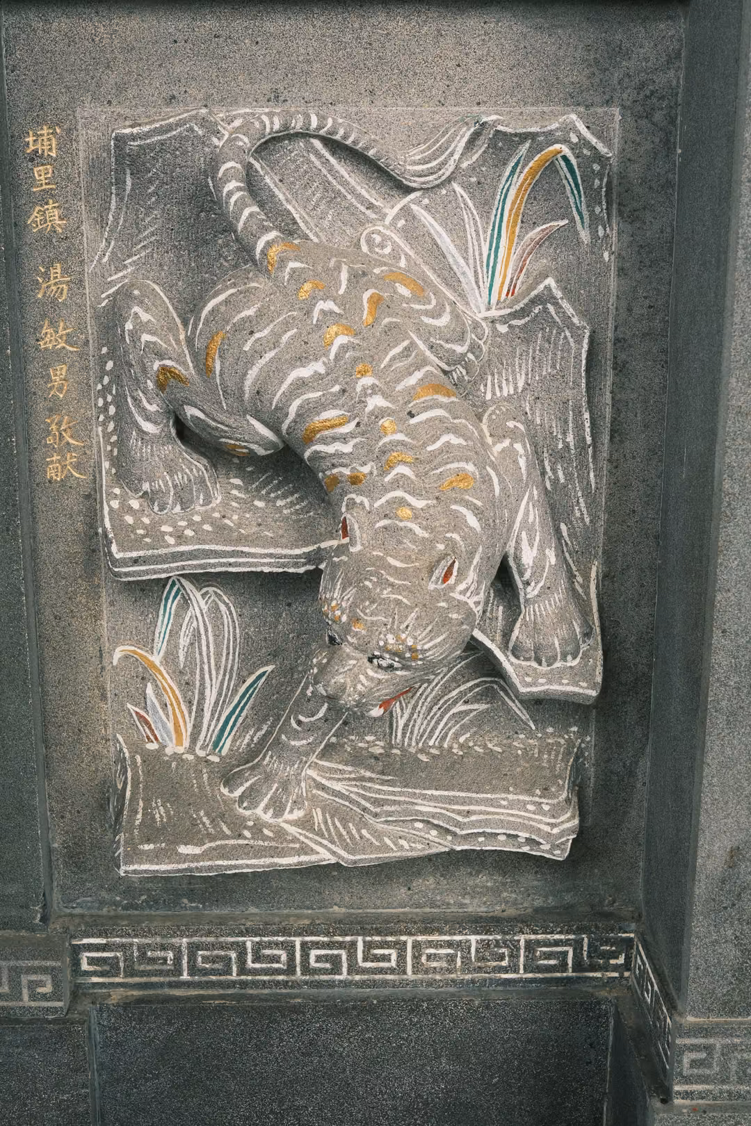 Stone relief of a striped tiger crouching down a slope through grass, gold characters on the side