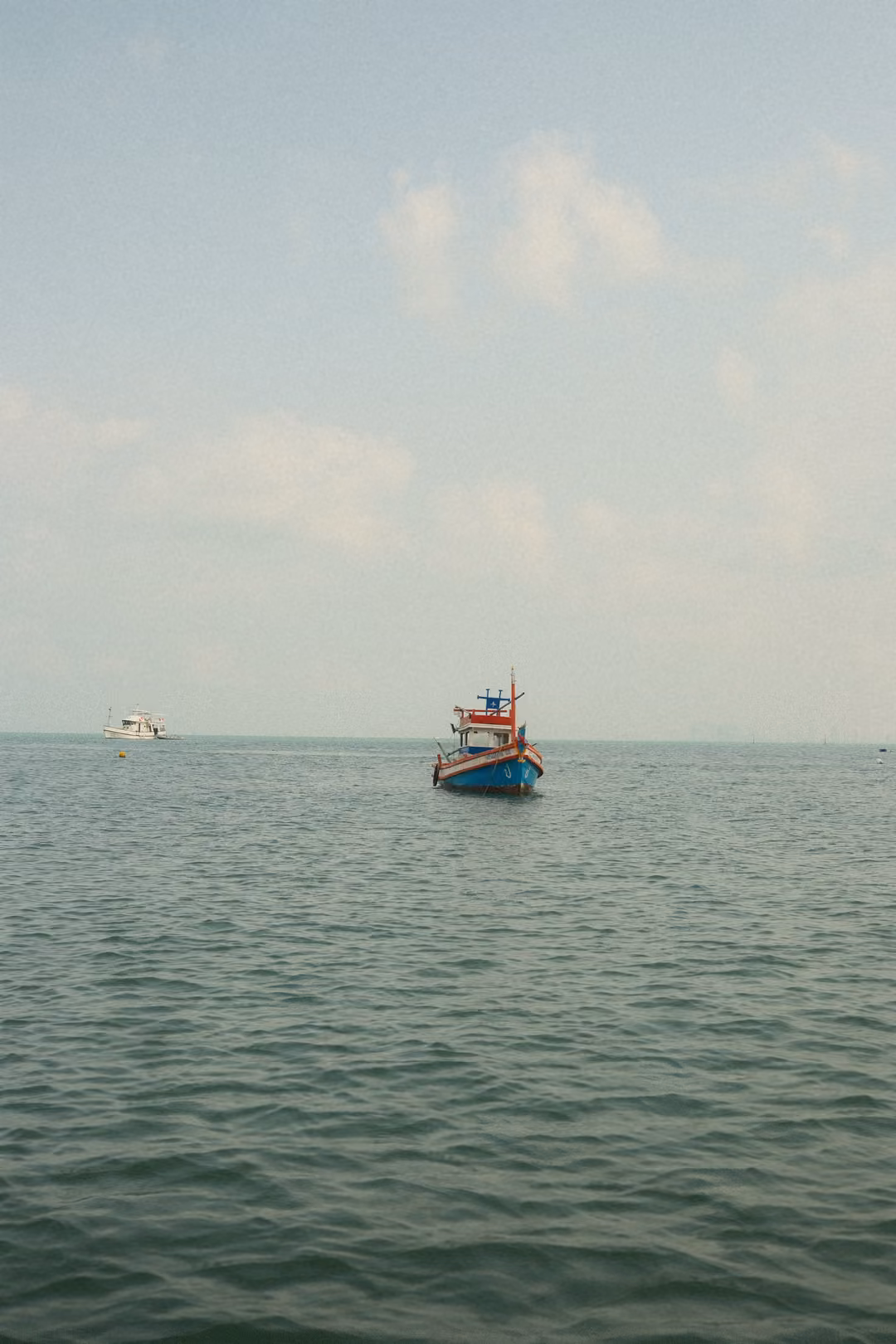 The painted fishing boat closer, with a white boat further off on the calm sea.