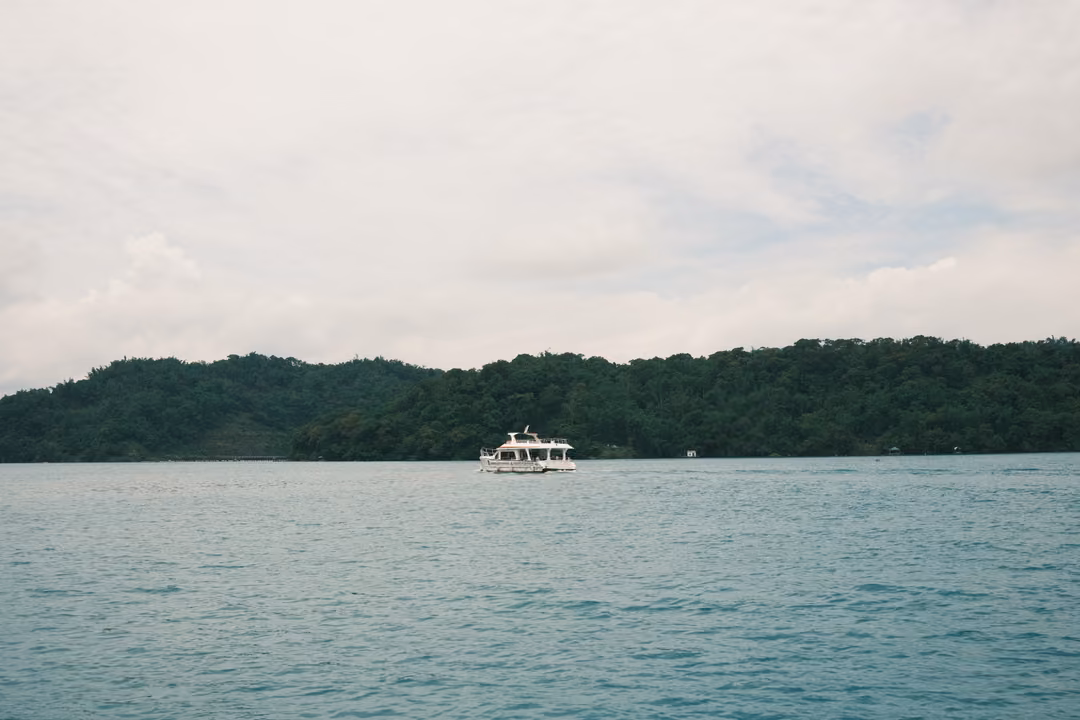 Small white boat on an open lake in front of a long low forested ridge under a pale sky