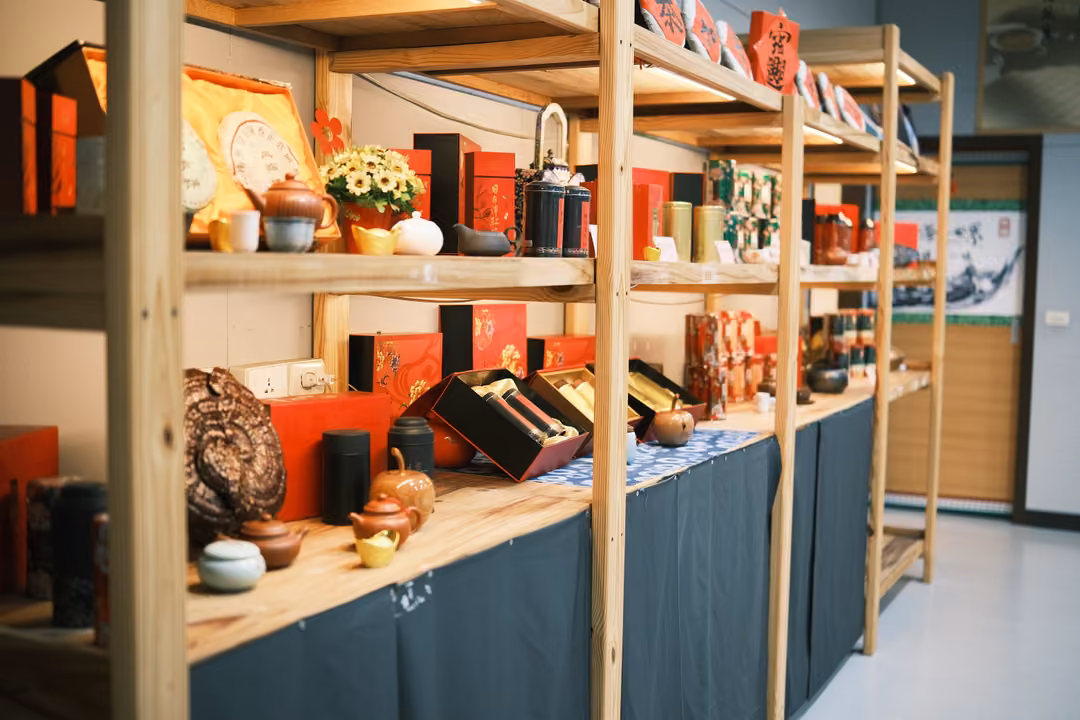 Wooden shelves stocked with teapots, red gift boxes, tins and a large round tea cake in a shop