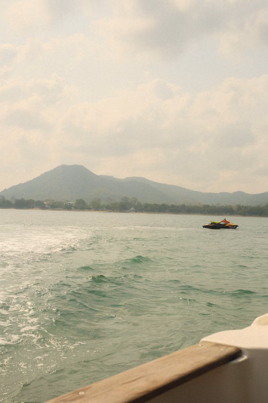 A green hill over a turquoise sea, a jet ski crossing in the distance, the boat's rail in the corner.