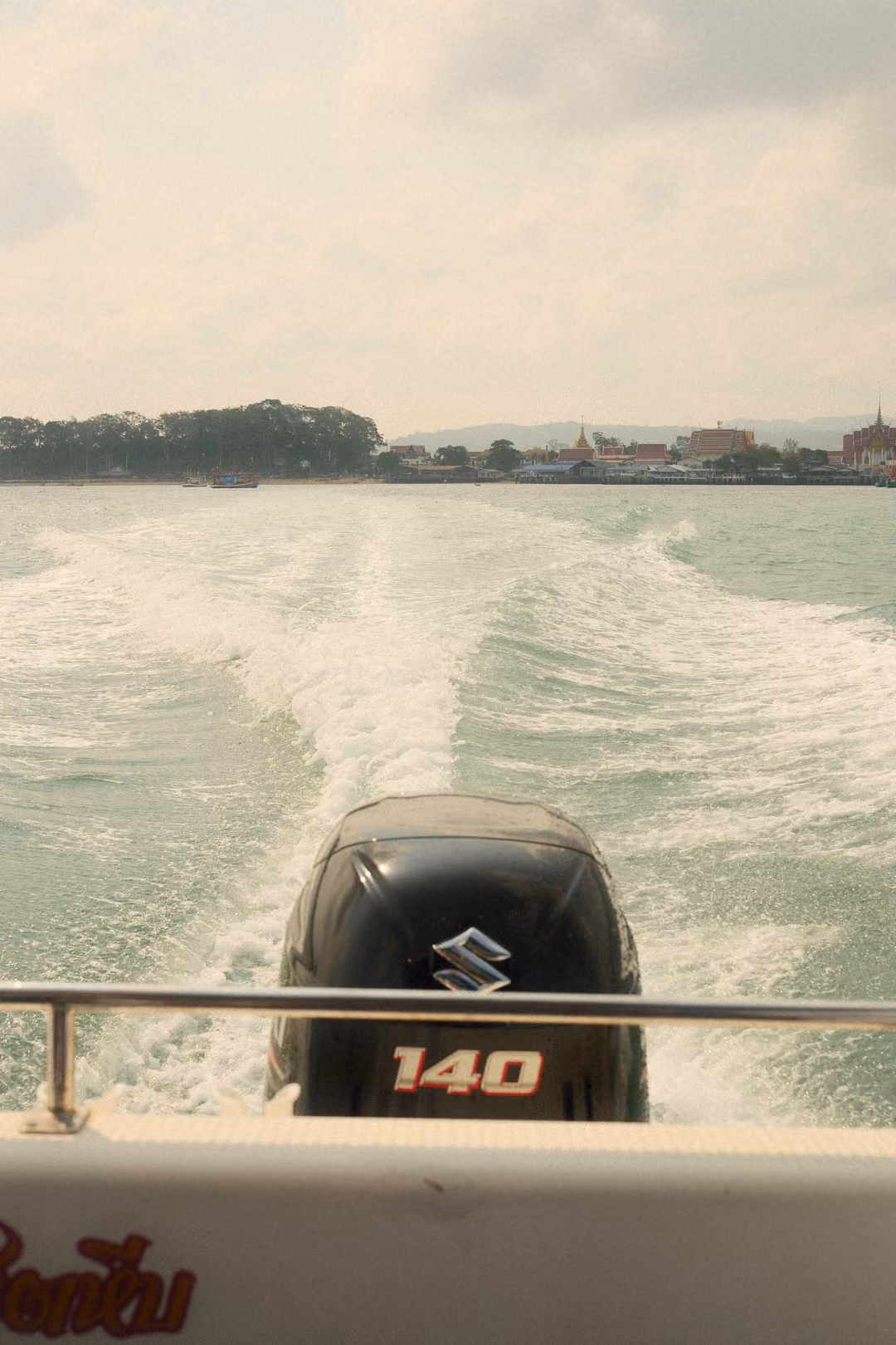 An outboard motor marked 140 at the stern, a wide white wake trailing back to the distant shore.