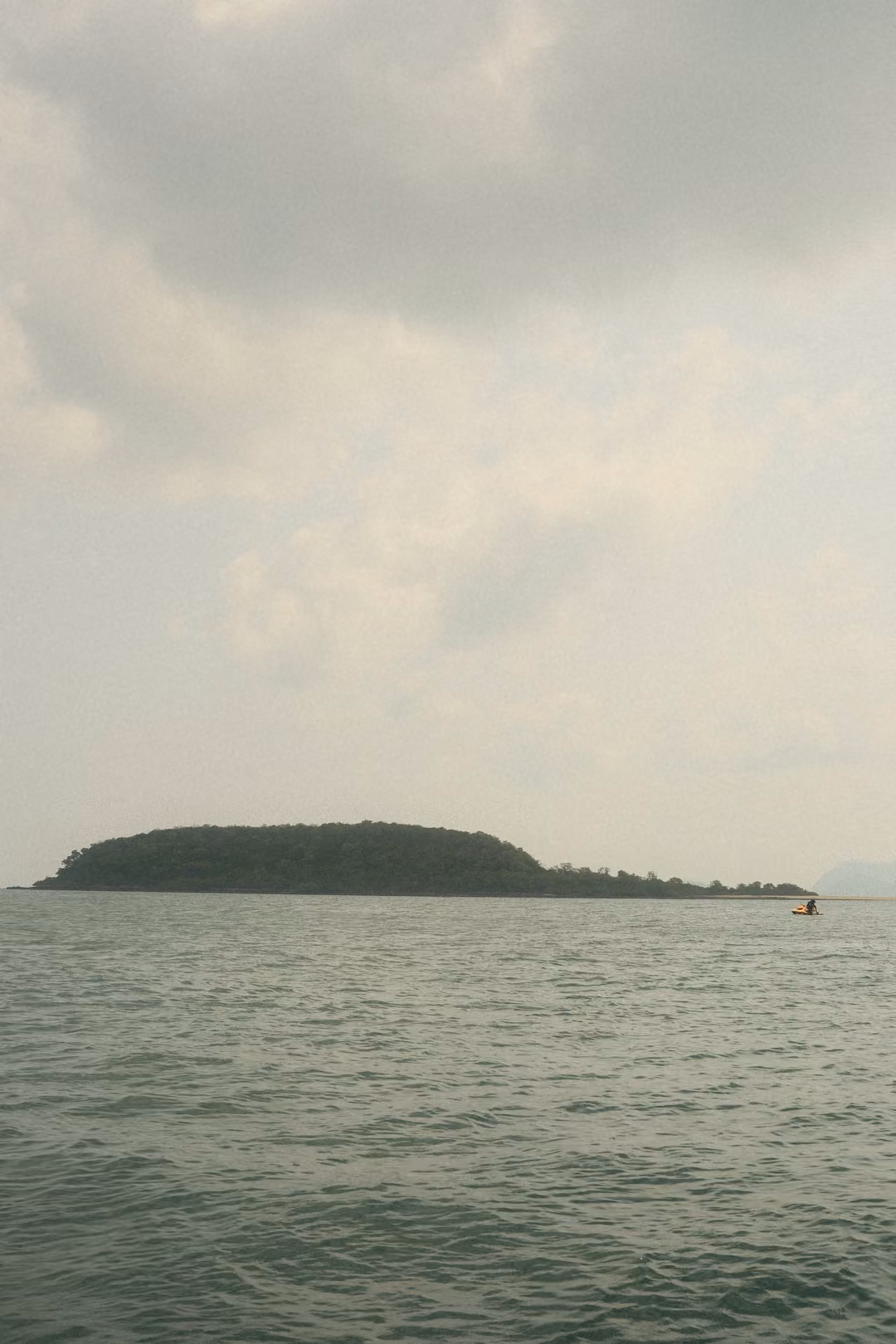 A low flat island under a pale, cloudy sky, with a small orange float on the grey-green sea.
