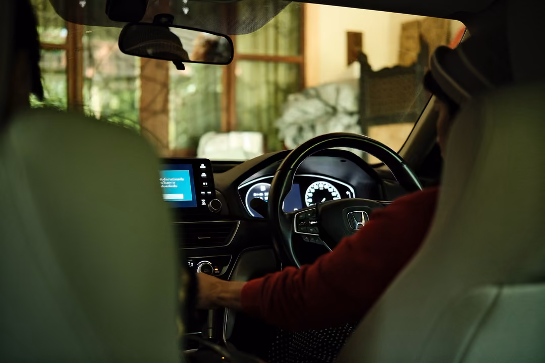 View from the back seat of a car interior, a driver's hand in a red sleeve on the steering wheel