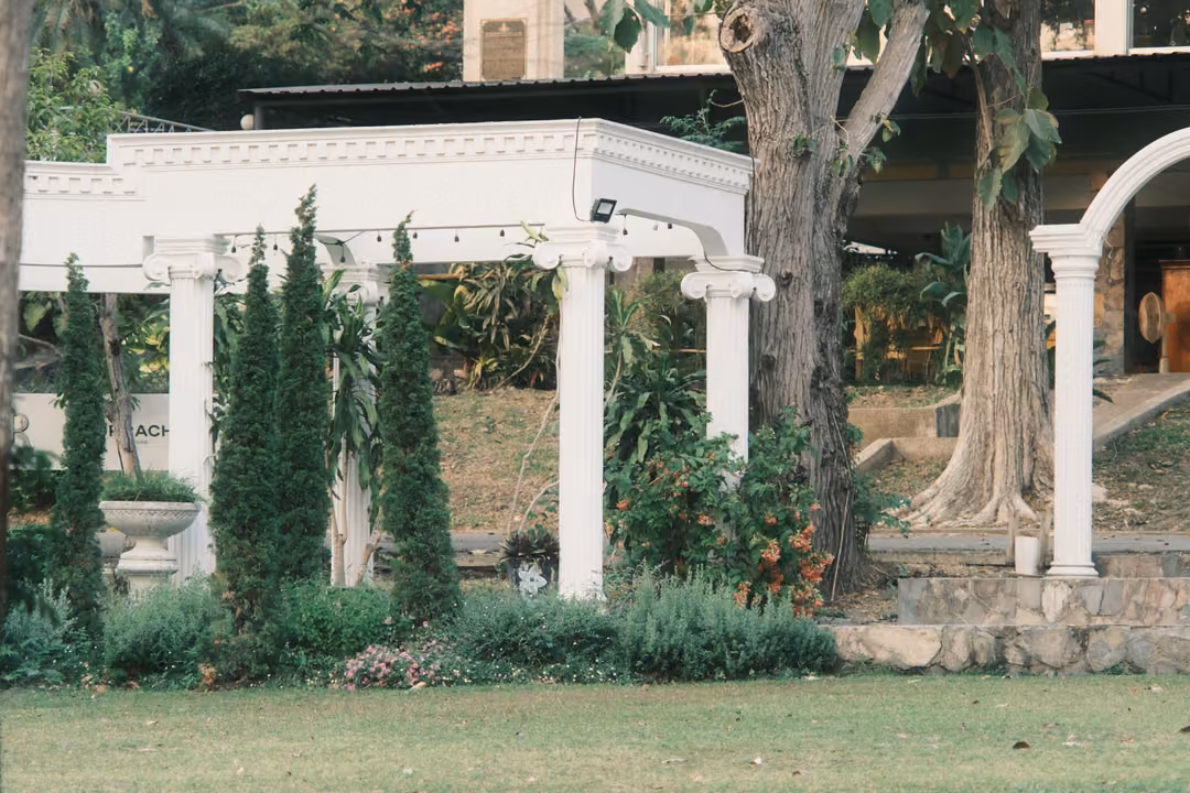 White classical colonnade with pillars and an arch in a garden of cypress trees and green lawn