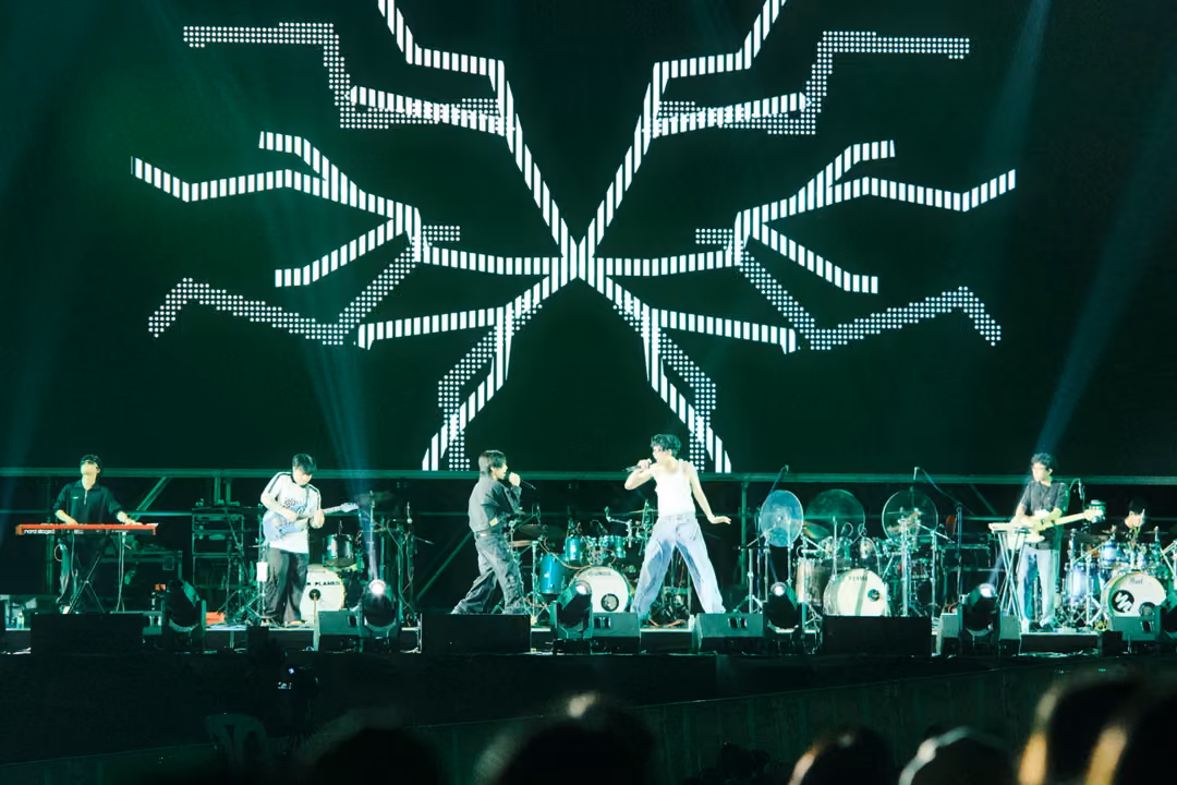 Band on a green stage below a screen of white dotted branching lines, the singer moving forward at centre.