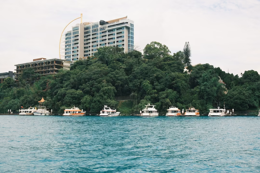 Bright turquoise lake in front of a forested shore with moored boats and a tall hotel tower behind
