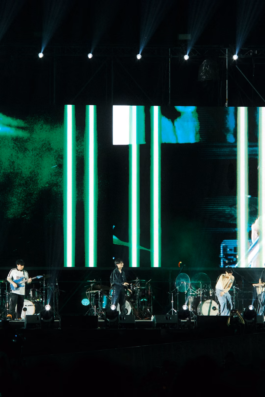 Vertical view of a stage with green vertical light bars and smoky green graphics on the screen, band below.
