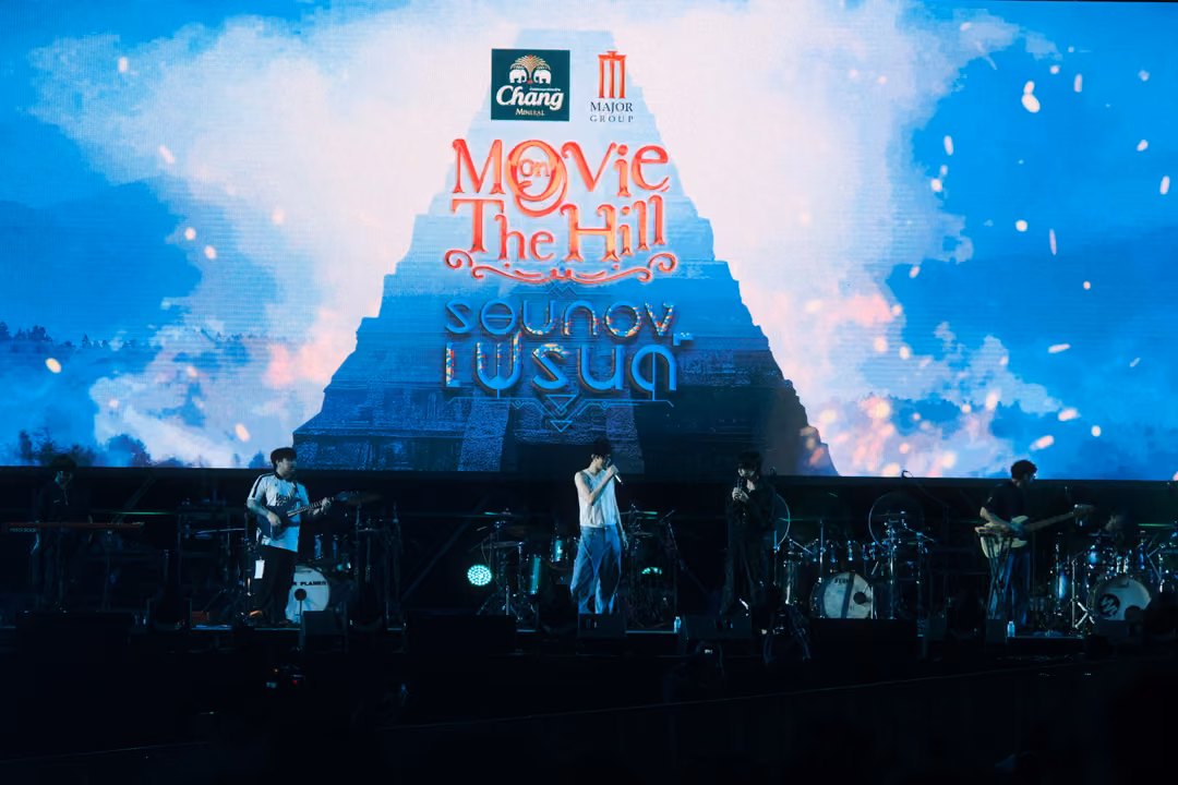 Screen showing the Movie on The Hill title over a stepped pyramid and clouds, band performing on the dark stage below.