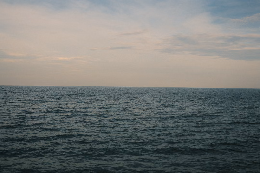 Calm blue-grey sea stretching to a flat horizon under a soft, cloudy evening sky