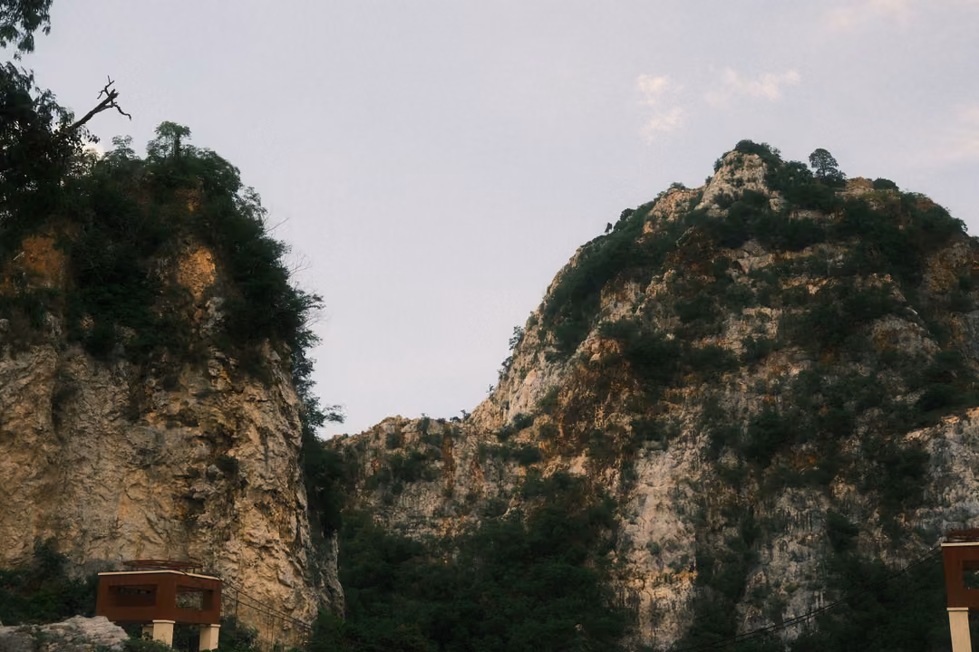 Two jagged limestone cliffs with patches of green under a pale sky, a small red sign stand below