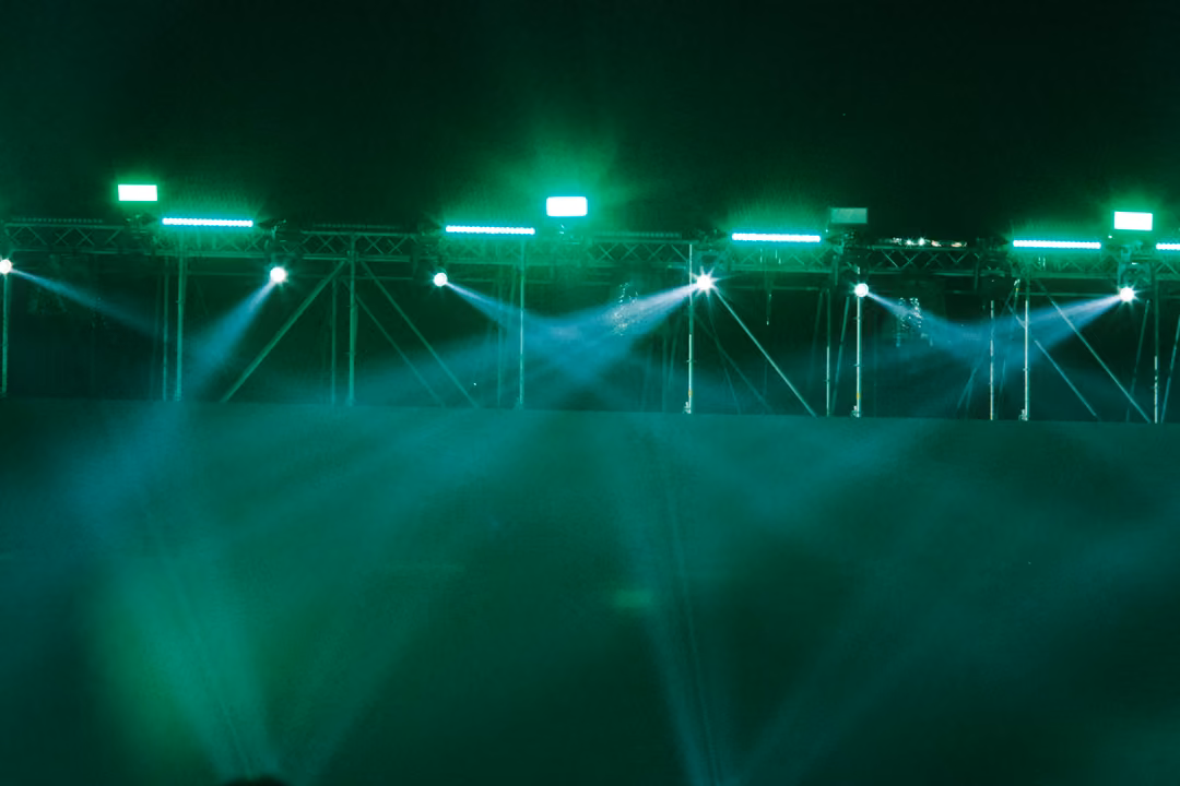 Green light beams fanning down from a steel truss into green haze, no performers visible