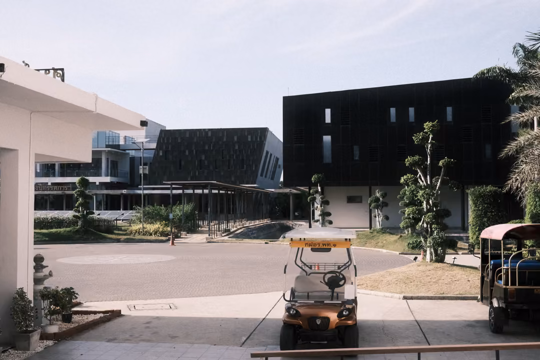 Paved courtyard with modern dark-panelled buildings, a small golf cart and a tuk-tuk parked near trees
