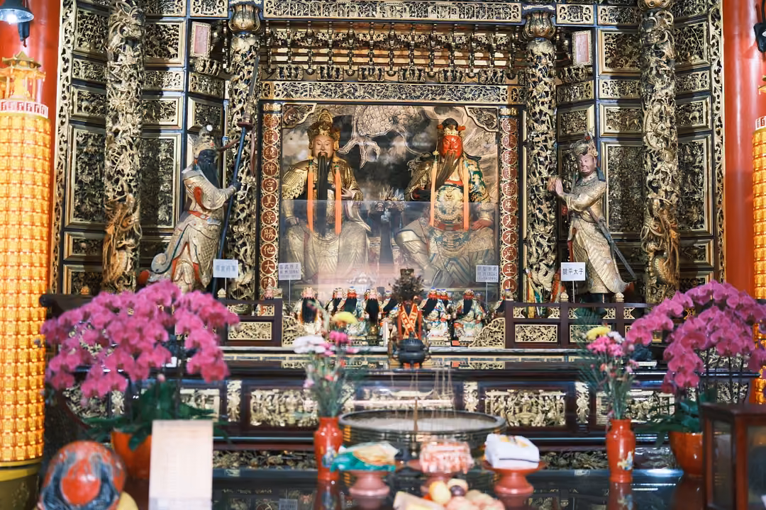 Altar with two seated figures in red and gold flanked by standing statues, magenta orchids in vases