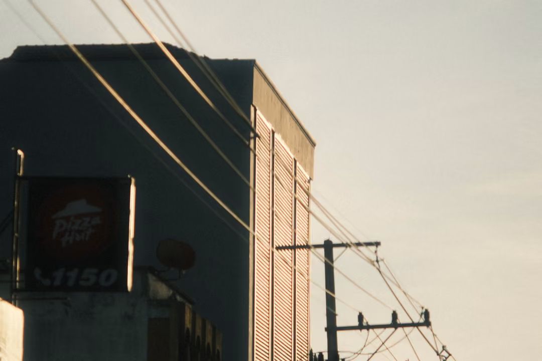 The upper corner of a building with a Pizza Hut sign and a 1150 phone number, crossed by power lines.
