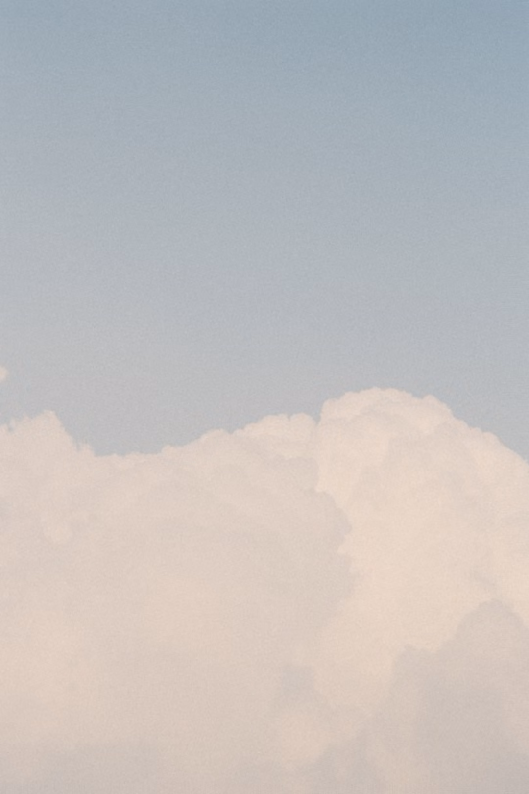 Soft white cumulus clouds rising against a pale blue-grey sky