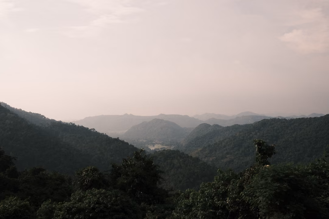 A wide view of dim, hazy mountain ridges and a forested valley in late afternoon.