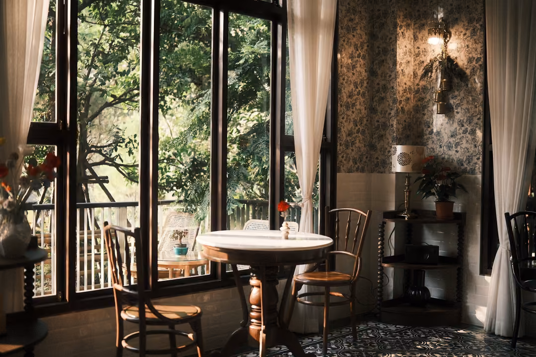 Nearly identical view of tall windows, round table, two chairs and patterned tile floor in late sun