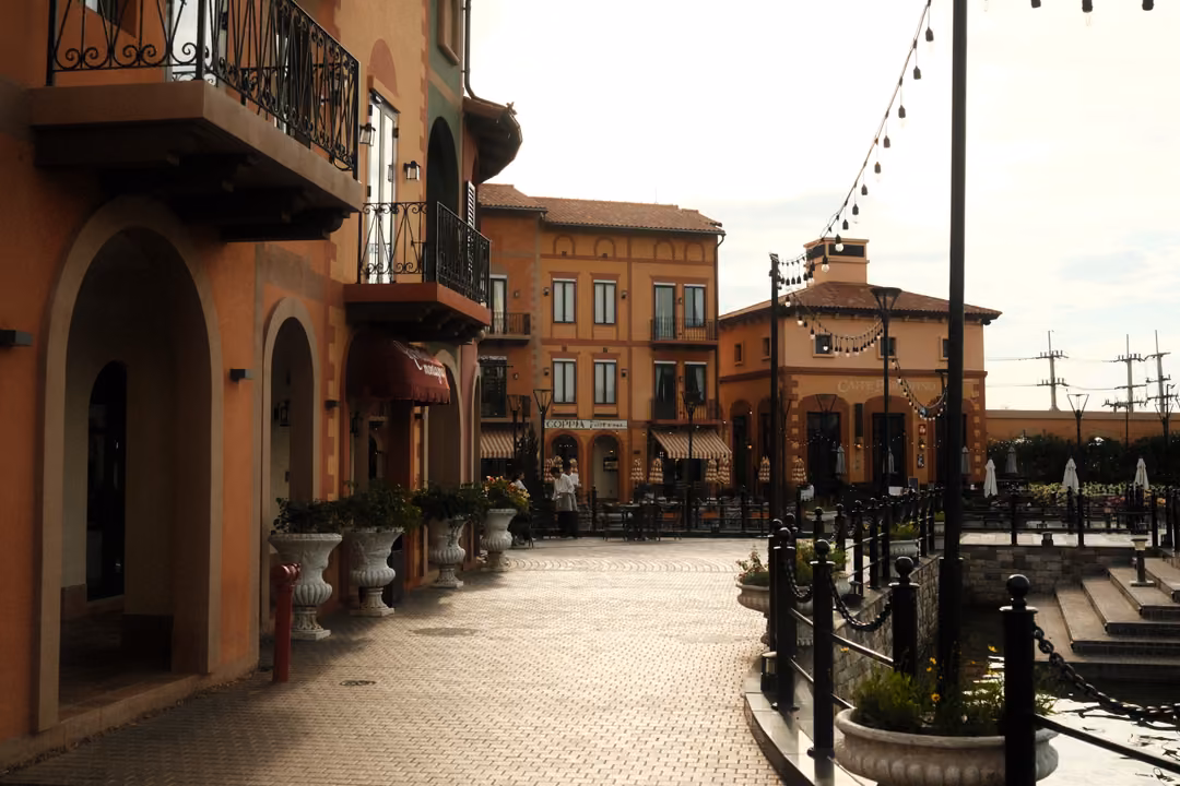 Terracotta arcades and balconies along a paved promenade with iron railings, planters and strung lights