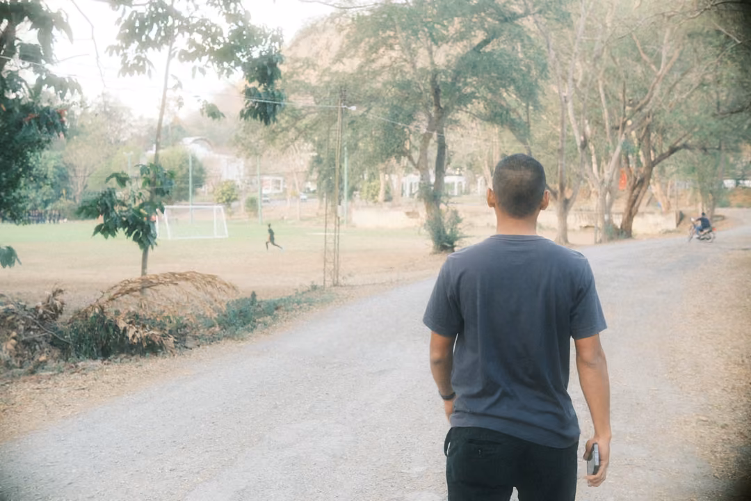 Man seen from behind on a road overlooking a field with football goals and scattered trees