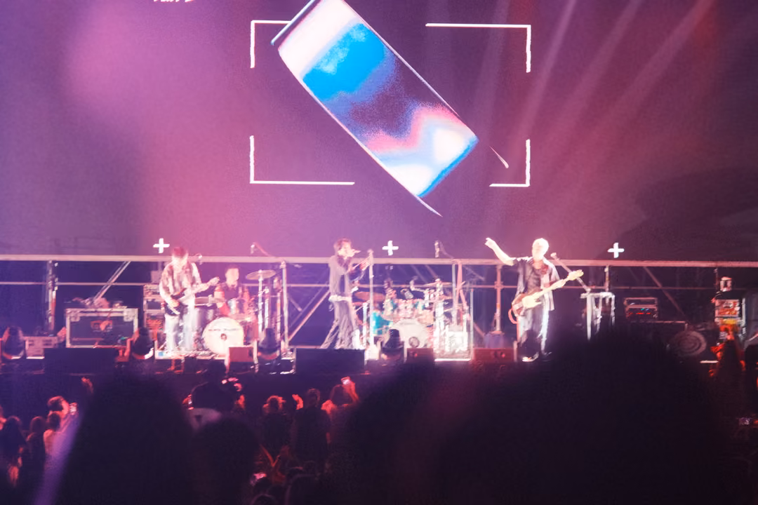 Band on a pink and purple stage beneath a screen showing a tilted glowing rectangle inside white corner brackets.