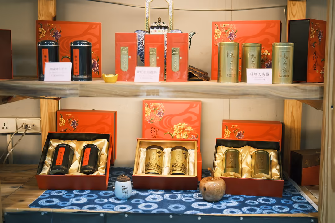 Display of red tea gift boxes with gold and black tins on shelves above a blue patterned cloth