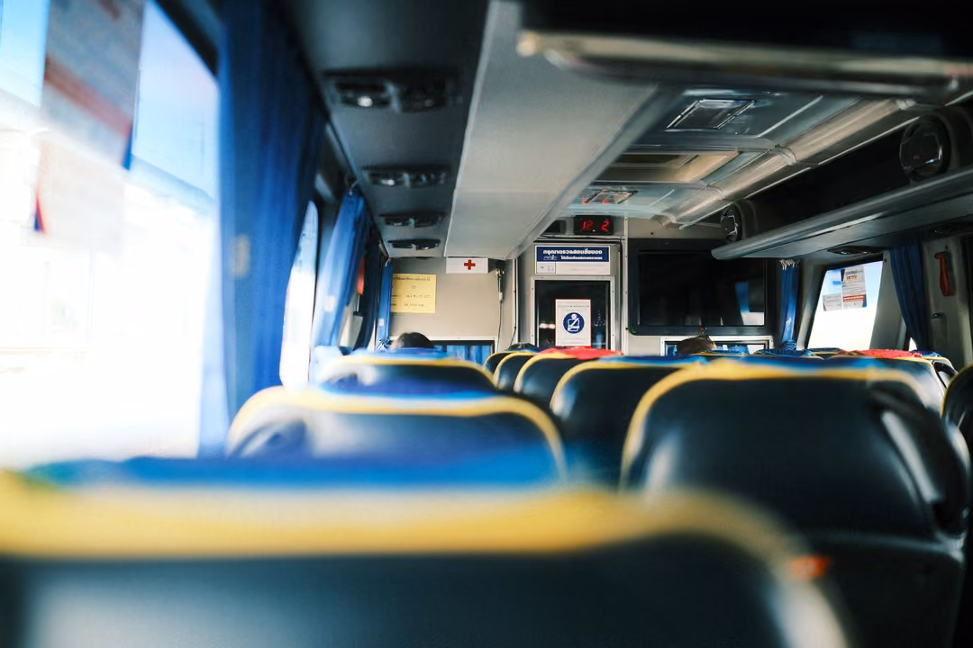 Inside a bus with rows of blue seats trimmed in yellow, blue curtains and a bright window on the left