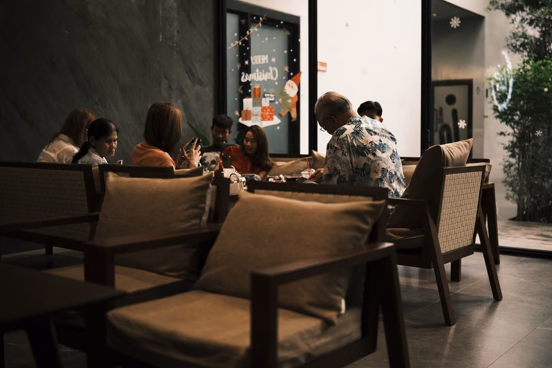 A café corner with dark walls and a glass door with a holiday greeting, people seated at tables.