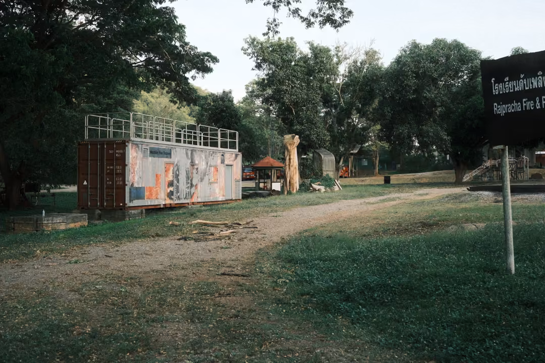 Painted container on a grassy field with a dirt track, carved wooden figure and a black sign at right