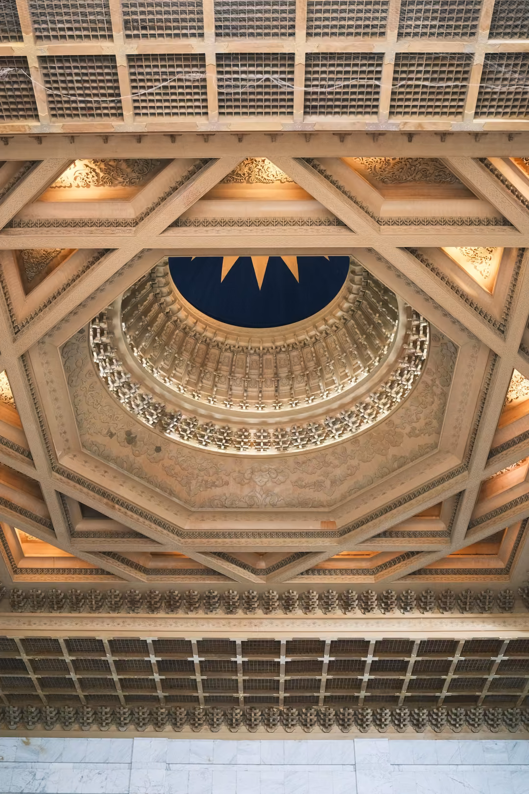 Looking up into an ornate octagonal ceiling with lit coffers, carved rings and a dark blue centre