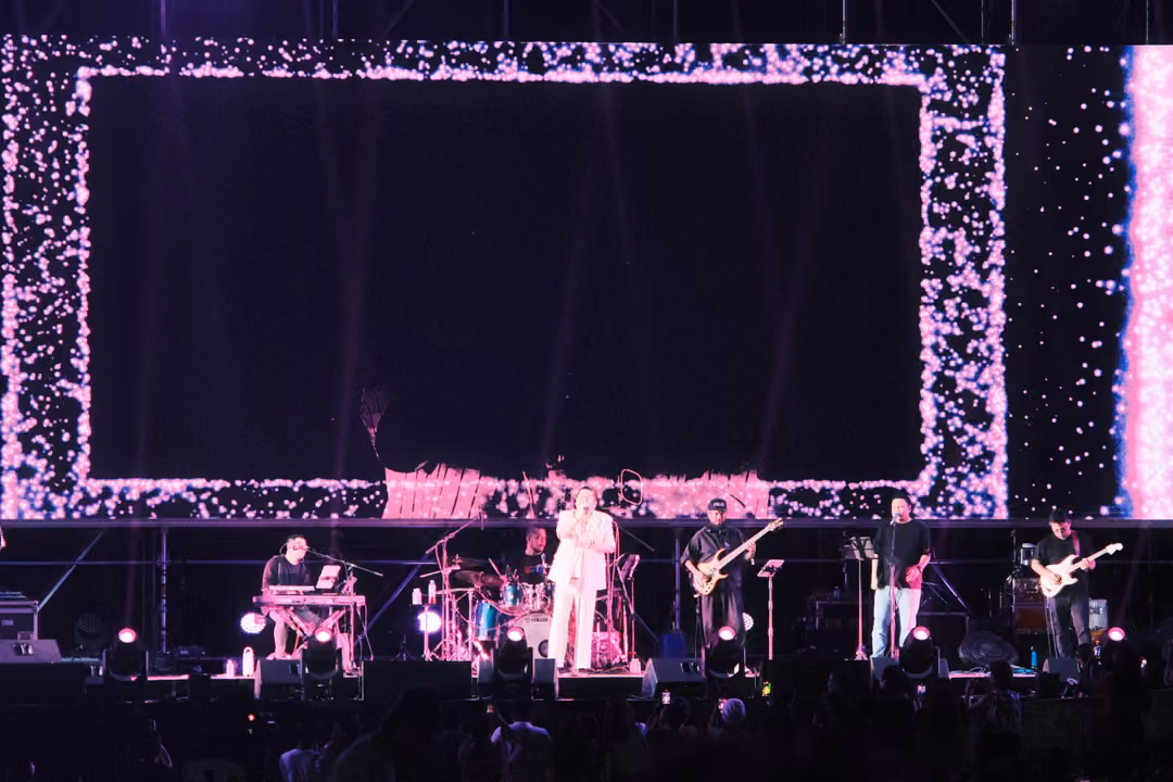 Band on stage below a large screen framed by pink and white glitter around a black rectangle