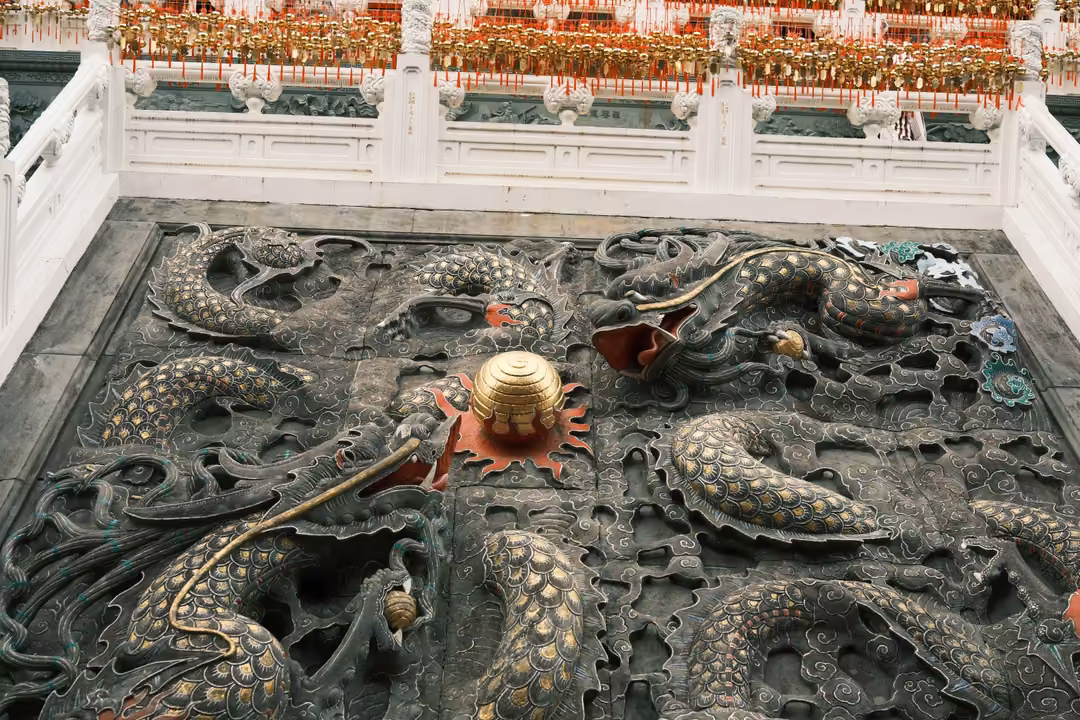 Large stone relief of dragons coiling around a golden orb set in a courtyard, white balustrades around it