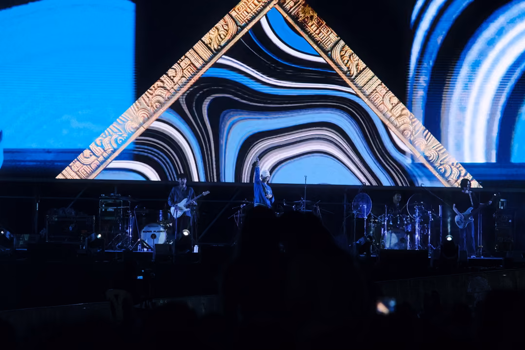 Stage with a large triangular frame of carved patterns around blue and white swirling stripes, band in dim light below.