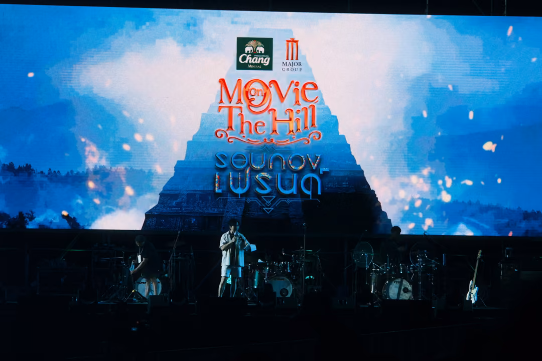 Screen with the Movie on The Hill title over a pyramid and clouds, a single performer standing on the dim stage below.