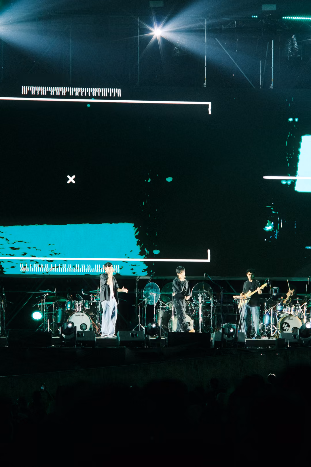 Stage at night with a mostly black screen, a white bracket and a turquoise slab, spotlights burning overhead.