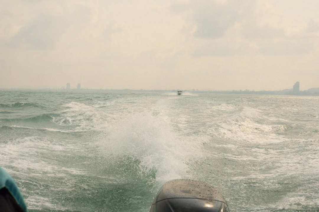 A white wake churning behind the boat's motor, a distant boat and faint skyline on the horizon.