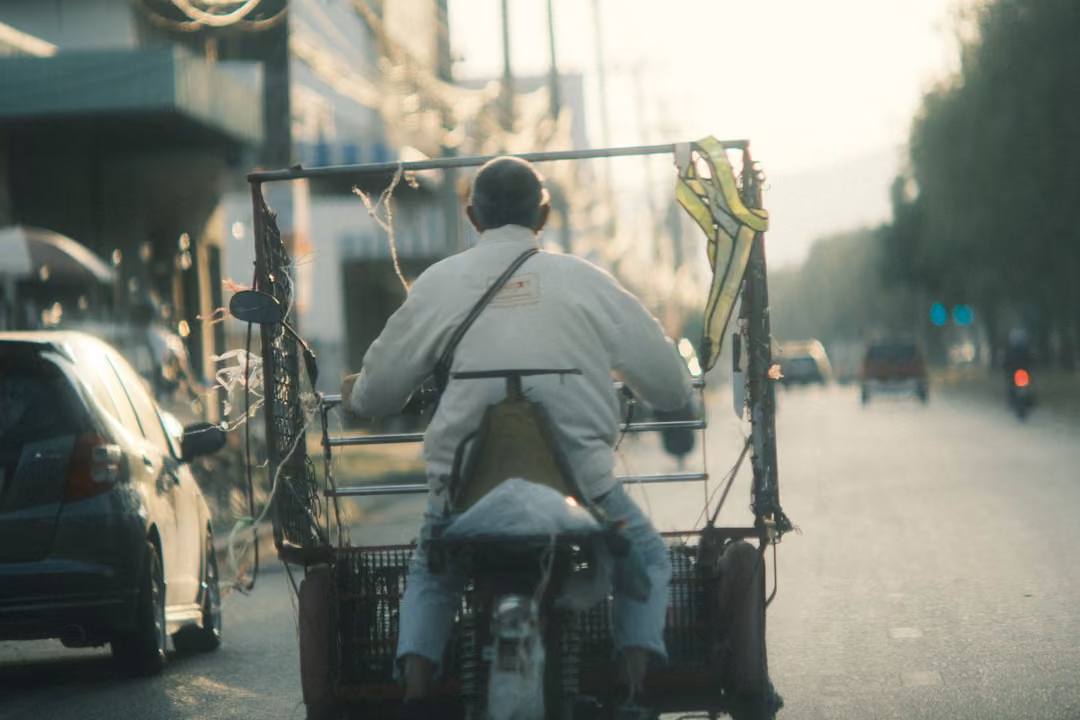 A rider in a white jacket on a motorbike pulling a cage-like cart with a yellow ribbon hanging from its frame.