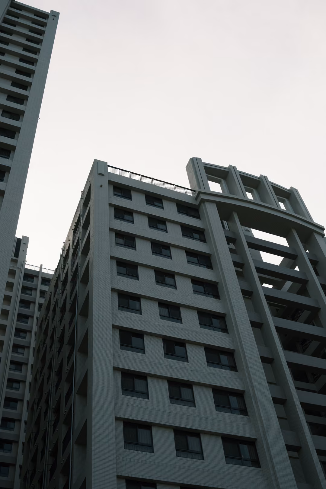 Grey high-rise apartment building seen from below against a pale overcast sky